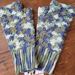 May include: A pair of fingerless gloves in a blue, green, and white crochet pattern. The gloves have a ribbed cuff.