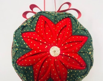 Puede incluir: Un adorno navideño de tela rojo y verde con forma de estrella y lunares dorados. El adorno está colgado de una cinta roja.
