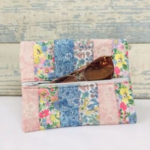 Może przedstawiać: Różowa i niebieska kosmetyczka z kwiatowym wzorem i zamkiem błyskawicznym, w środku znajdują się okulary przeciwsłoneczne.