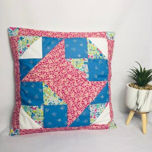 Könnte beinhalten: Ein quadratisches Patchwork-Kissen in Rosa und Blau mit einem Blumenmuster. Das Kissen hat einen weißen Rand.