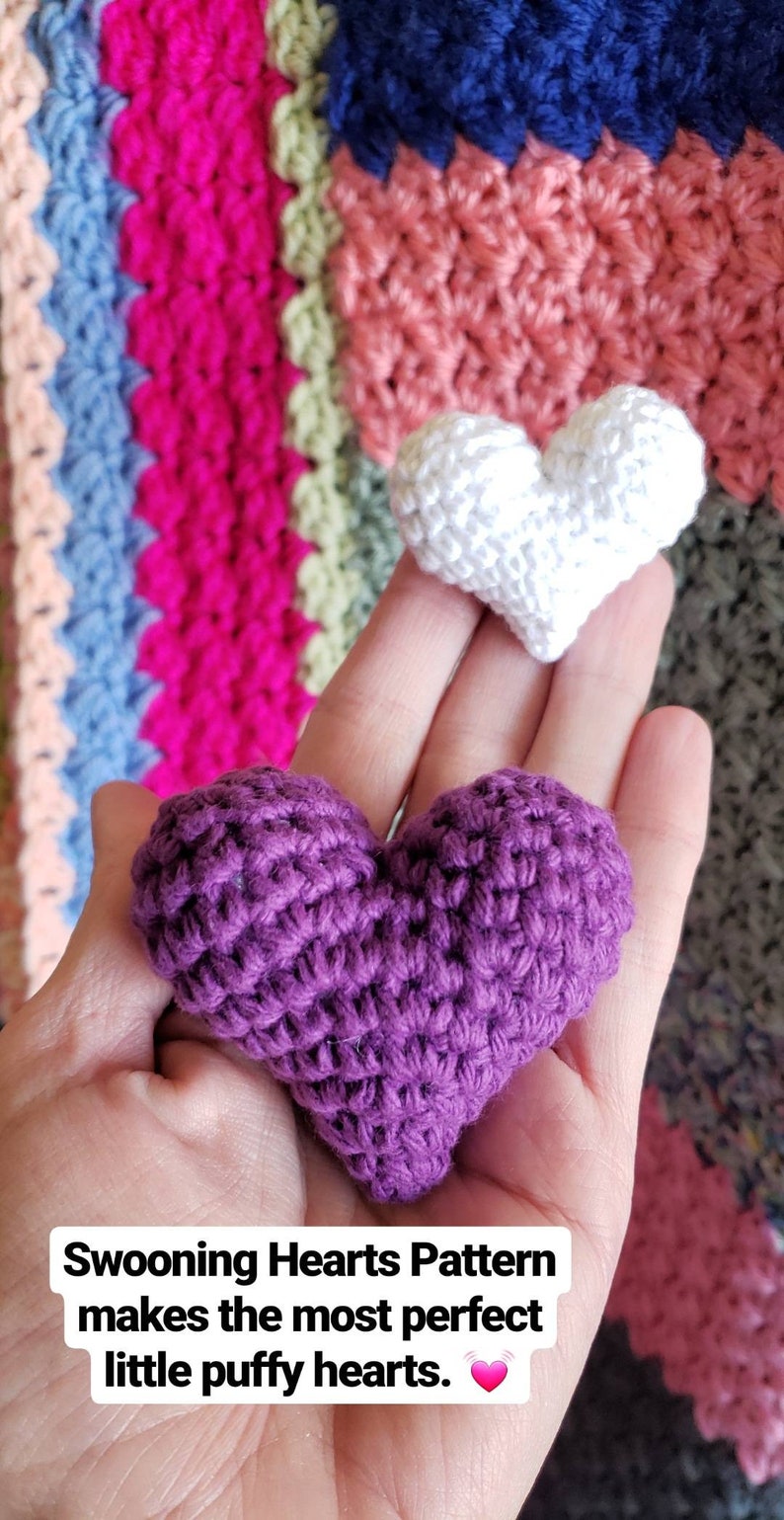 Puede incluir: Dos corazones tejidos a crochet, uno morado y otro blanco, se sostienen en una mano. El texto "Swooning Hearts Pattern makes the most perfect little puffy hearts." est&aacute; debajo de los corazones.