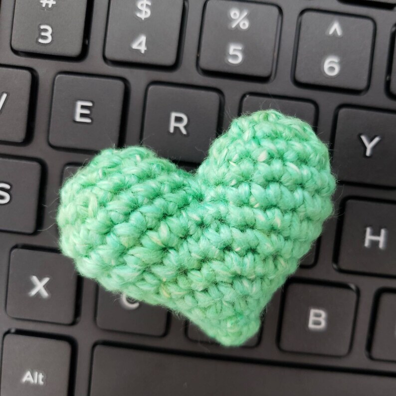 Puede incluir: Un coraz&oacute;n de crochet verde sobre un teclado negro.