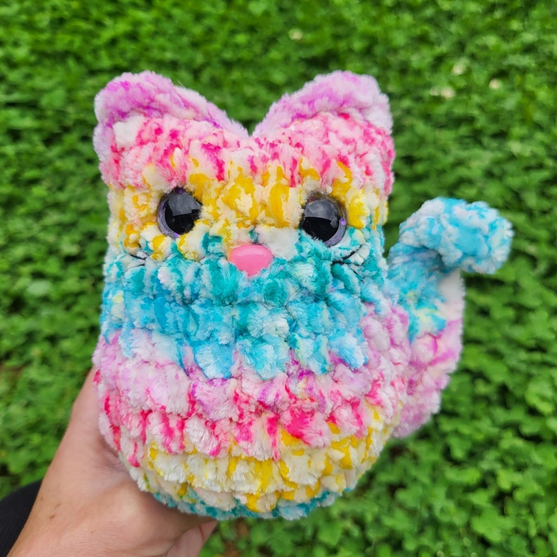 May include: A colorful crocheted cat toy with pink, blue, yellow, and white yarn. The cat has black eyes and a pink nose.