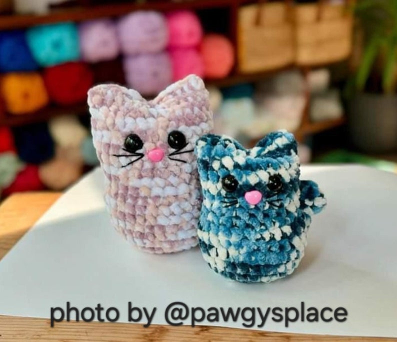 May include: Two crocheted cat toys, one pink and white and one blue and white. The toys have black eyes and pink noses.