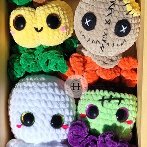 May include: A set of five crocheted Halloween-themed plush toys in a wooden box. The toys include a pumpkin, a ghost, a Frankenstein, a voodoo doll, and a purple monster.