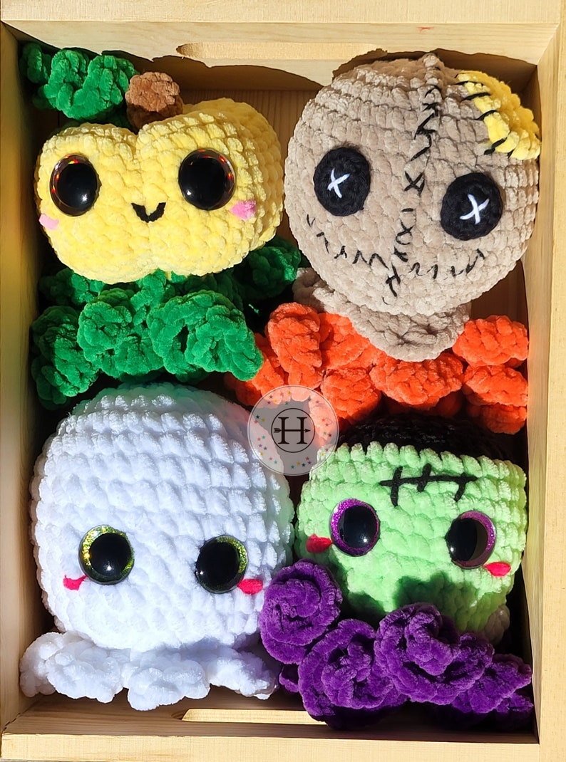May include: A set of five crocheted Halloween-themed plush toys in a wooden box. The toys include a pumpkin, a ghost, a Frankenstein, a voodoo doll, and a purple monster.