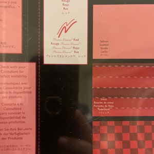 May include: A close-up of a color chart with different shades of red. The chart includes the words "Red", "Rouge", "Rojo", "Rot", and "レッド" in multiple languages. The chart also includes the words "Salmon", "Saumon", "Sandia", "Lachs", and "サーモン" in multiple languages. The chart also includes the words "Stitch", "Boucles de m&eacute;tal", "Puntadas de Rojo", "Fadenstich", and "スティッチ" in multiple languages. The chart also includes the words "Weave", "Ondulation", "Cuadros de Rojo", "Stoffkaro", and "ウィープ" in multiple languages.