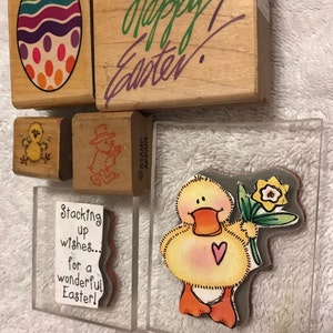 May include: A set of six rubber stamps with Easter themes. The stamps feature a colorful Easter egg, a chick, a duckling, and the words "Happy Easter!" and "Stacking up wishes... for a wonderful Easter!"