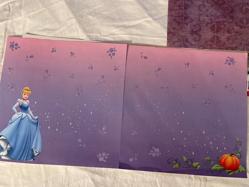 May include: A purple and pink gradient scrapbook paper with a Cinderella illustration on the left side and a pumpkin vine on the right side. The paper is decorated with small white stars and purple flowers.
