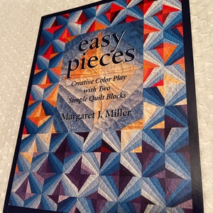 May include: Book cover with the title "easy pieces" in white text on a blue background. The subtitle is "Creative Color Play with Two Simple Quilt Blocks" and the author is "Margaret J. Miller". The cover features a quilt pattern with blue, purple, orange, and red triangles.