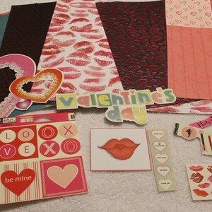 May include: A collection of Valentine's Day themed craft supplies. Includes heart-shaped cutouts, stickers, patterned paper with lips and hearts, and the words "Valentine's Day" and "Love". Colors include red, pink, white, and teal.