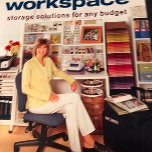 May include: A woman sits in a chair in front of a well-organized craft room. The room has shelves filled with colorful paper, craft supplies, and storage containers. The text on the cover of the book reads "How to organize your scrapbook workspace storage solutions for any budget".