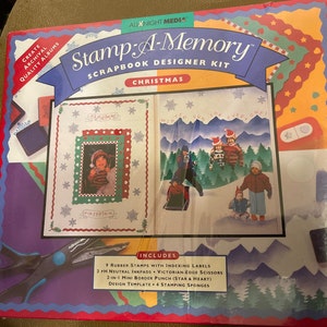 May include: A Stamp-A-Memory scrapbook designer kit for Christmas. The box features a red, white, and green color scheme with a winter scene on the front. The kit includes 9 rubber stamps, 3 inkpads, Victorian edge scissors, a 2-in-1 mini border punch, a design template, and 4 stamping sponges.