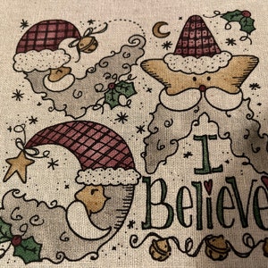 May include: A beige fabric with a Christmas-themed design featuring three Santa Clauses with red hats and white beards. The text "I Believe!" is written in green and red letters.