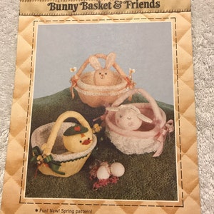 May include: A craft pattern titled "Bunny Basket & Friends" featuring three Easter-themed basket designs: a bunny, a duck, and a lamb. The pattern includes full-size pieces and is suitable for Easter, nurseries, or children's rooms. The cover has a quilted design.