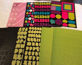 May include: Assortment of alphabet and number stickers in various colors. The stickers are on black and green sheets. The numbers are 0-6 and the letters are in uppercase.
