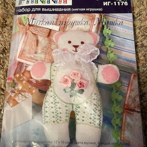 May include: A white teddy bear embroidery kit with pink accents and a floral design. The kit includes 3 colors of embroidery floss, 6 types of ribbon, beads, and instructions. The finished project will be 12 inches by 16 inches.