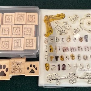 May include: A collection of wooden stamps and clear stamps. The wooden stamps include holiday-themed images and phrases. The clear stamps include letters, numbers, and decorative elements. The stamps are stored in clear plastic containers.