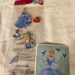 May include: A set of Cinderella stickers featuring a blue dress, a pumpkin, a glass slipper, and a sticker sheet with Cinderella and birds. The sticker sheet has the text "Cinderella" and "&copy;Disney".