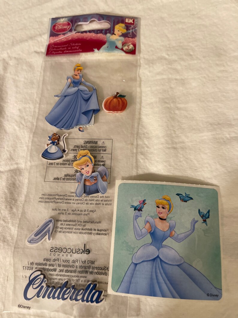 May include: A set of Cinderella stickers featuring a blue dress, a pumpkin, a glass slipper, and a sticker sheet with Cinderella and birds. The sticker sheet has the text "Cinderella" and "&copy;Disney".