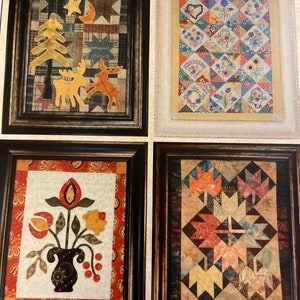 May include: Four framed quilts depicting the four seasons. The top left quilt features a yellow tree, a crescent moon, and two reindeer on a patchwork background. The top right quilt features a colorful patchwork design with floral motifs. The bottom left quilt features a vase of flowers with red, yellow, and green accents. The bottom right quilt features a patchwork design with autumn leaves in shades of red, orange, and yellow.