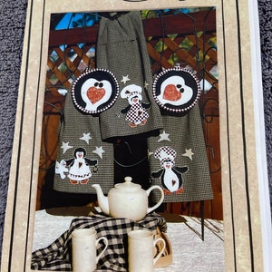 May include: A set of three black and white kitchen towels with penguin appliques and two matching pot holders. The towels feature a black and white checkered pattern with red hearts and white stars. The pot holders are round and feature a penguin with a red heart and white stars. The text on the image reads "#504 Penguin Party Kitchen Set© Three Appliquéd Towels & Two Pot Holders".