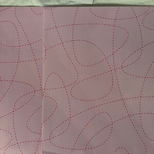 May include: A pink sheet of paper with a pattern of red dashed lines forming abstract shapes.
