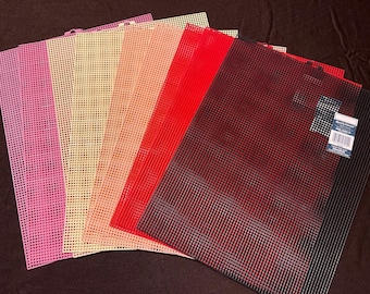 May include: A collection of colorful plastic canvas sheets in shades of pink, cream, peach, red, and black. The sheets are arranged in a fan shape, showcasing their grid-like structure. Ideal for various crafting projects.