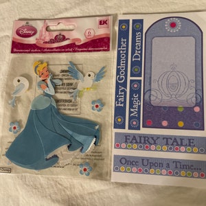 May include: A set of six dimensional Cinderella stickers featuring Cinderella, a carriage, and birds. The stickers are on a clear plastic sheet with a pink and white background. The text "Fairy Godmother Magic Dreams" and "Fairy Tale Once Upon a Time..." is printed on the sheet.