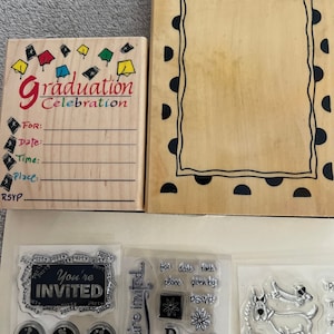 May include: A set of wooden rubber stamps for crafting and scrapbooking. The stamps feature graduation themes, including a graduation cap, the words "Graduation Celebration", and a blank frame. There are also stamps with the words "You're Invited", "Party", and "Hop on over".