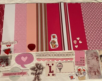May include: A collection of Valentine's Day themed craft supplies, including patterned paper, stickers, and embellishments. The supplies are arranged on a white surface and feature hearts, the words "Be Mine", and "Sweethearts".