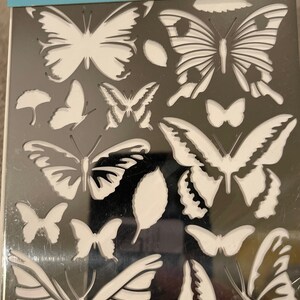 May include: Martha Stewart Crafts dry embossing stencil featuring various butterfly designs. The stencil includes multiple butterfly shapes and leaf shapes. The package is white and gray with the Martha Stewart Crafts logo.