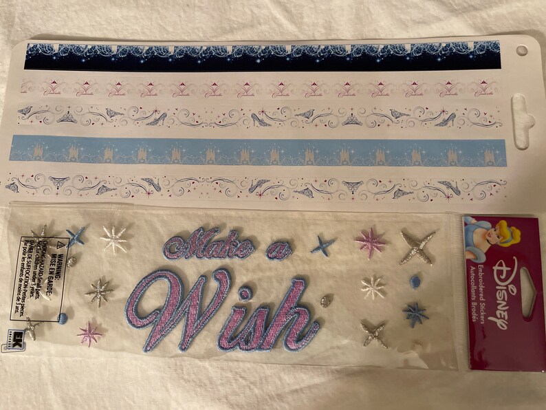 May include: A sheet of Disney princess themed stickers with a variety of designs, including castles, crowns, and stars. The stickers are embroidered and have a pink and blue color scheme. The sheet also includes the text "Make a Wish".