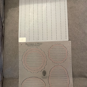 May include: A clear plastic stencil with four different shapes: a circle, a circle with a scalloped edge, an oval, and a circle with a scalloped edge. The stencil is labeled "Patterns 'N Pens" and "Patrones y Plumas".