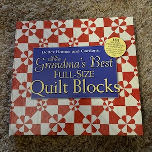 May include: A square book titled "Grandma's Best Full-Size Quilt Blocks" by Better Homes and Gardens. The cover features a red and white floral pattern and text in blue and gold. The book promises 101 blocks, borders, and bindings with over 5,000 interchangeable combinations.