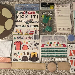 May include: A collection of soccer-themed craft supplies, including stickers, a calendar, a wooden soccer ball, and paper cutouts. The stickers feature soccer players, goals, and other soccer-related imagery. The calendar has a space for each month and special events. The wooden soccer ball is brown and white with a textured surface. The paper cutouts are in various colors and feature soccer-related designs.