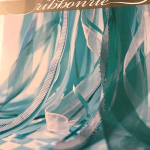 May include: An image featuring various ribbons in shades of teal, white, and blue. The ribbons are layered and flowing, with some having decorative edges. The word "ribbonrie" is displayed in a cursive font. The bottom of the image includes text about scrapbooking, cardmaking, home décor, and gifts.