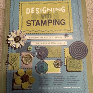May include: A book titled "Designing with Stamping: Bringing the art of stamping to the world of scrapbooking" with a blue and green cover featuring a variety of paper crafts and embellishments. The book includes a bonus CD.