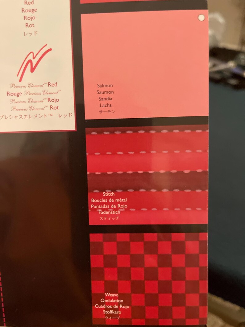May include: A color chart featuring various shades of red, including salmon. The chart displays different textures and patterns, such as stitching and a checkered weave, with corresponding color names in multiple languages.