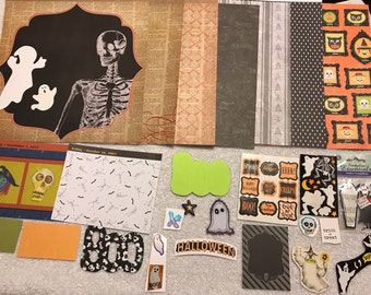 May include: A collection of Halloween themed scrapbook paper, stickers, and embellishments. The paper features a variety of patterns, including skeletons, ghosts, bats, and pumpkins. The stickers and embellishments include a variety of designs, such as ghosts, bats, pumpkins, and skulls.