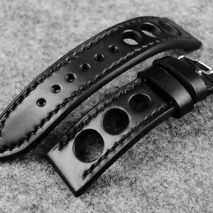 May include: Black leather watch strap with a perforated design and white stitching. The strap has a buckle closure.