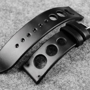 May include: Black leather watch strap with a perforated design. The strap has a buckle closure and is made of high-quality leather.