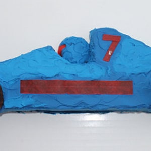 May include: A blue and brown race car cake decorated with red icing. The car has the number "7" on the side.