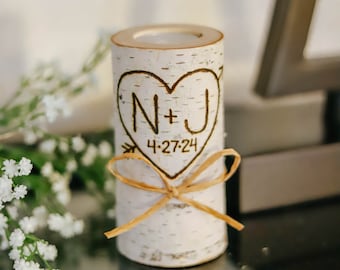 Puede incluir: Un portavelas de madera de abedul blanco con un diseño de corazón y las iniciales N+J y la fecha 4-27-24 grabadas en él. El portavelas está atado con una cinta marrón.