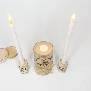 A personalized last name rustic birchwood wedding unity candle set. The centerpiece candle features a custom-engraved last name with a date and is surrounded by two smaller candles with an initial of the name.