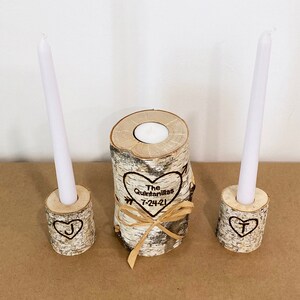 A personalized last name rustic birchwood wedding unity candle set. The centerpiece candle features a custom-engraved last name with a date and is surrounded by two smaller candles with an initial of the name.