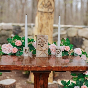 A personalized last name rustic birchwood wedding unity candle set. The centerpiece candle features a custom-engraved last name with a date and is surrounded by two smaller candles with an initial of the name.