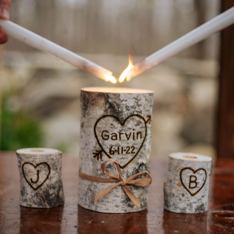 A personalized last name rustic birchwood wedding unity candle set. The centerpiece candle features a custom-engraved last name with a date and is surrounded by two smaller candles with an initial of the name.