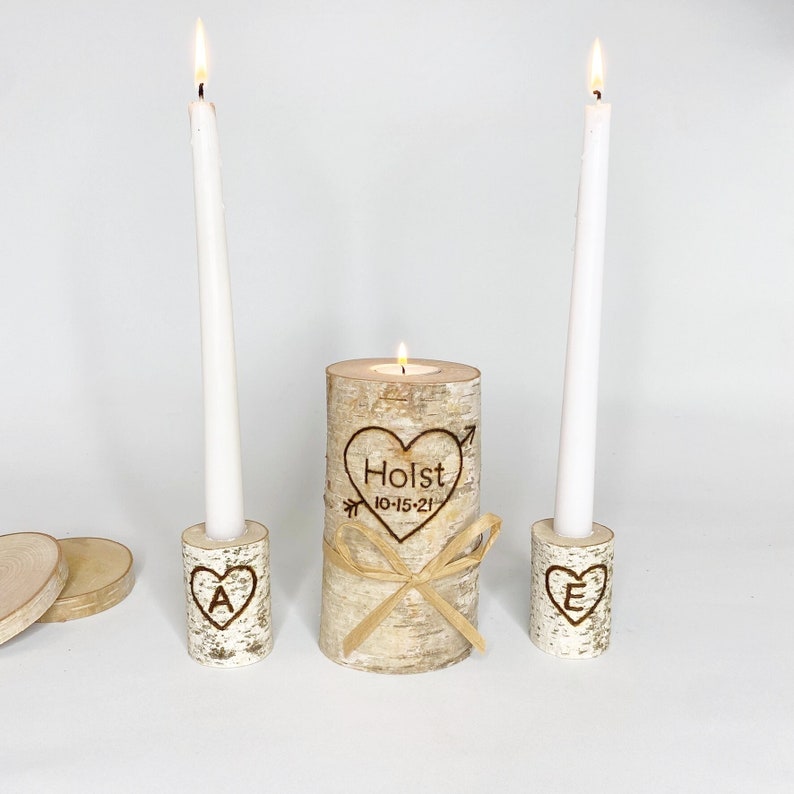 A personalized last name rustic birchwood wedding unity candle set. The centerpiece candle features a custom-engraved last name with a date and is surrounded by two smaller candles with an initial of the name.