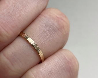 May include: A close-up of a gold hammered band ring worn on a finger.